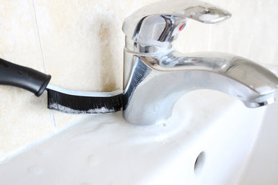 A crevice brush cleans behind a bathroom sink tap
