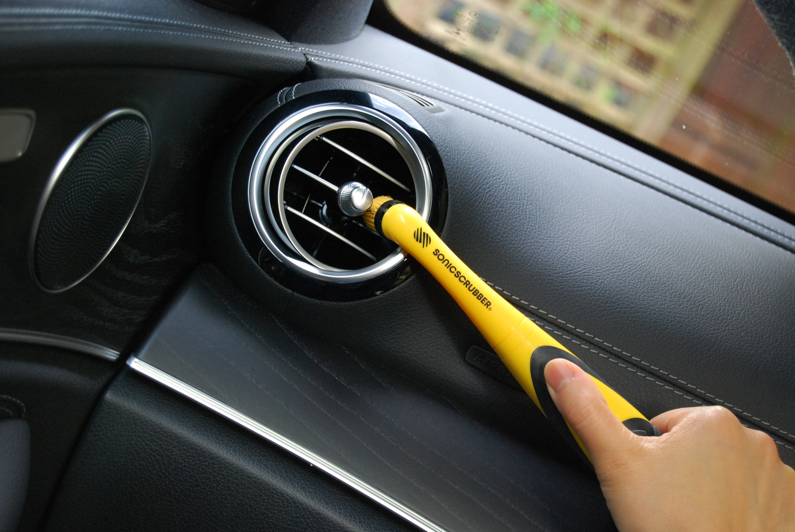 Yellow SonicScrubber electric cleaning brush being used to clean a car dashboard.